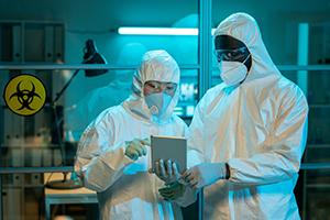 Two people in hazmat suits in a lab with biosafety sign behind them.